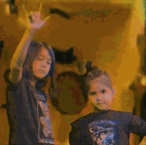 two kids in baby teith tees, one throwing up rock horns